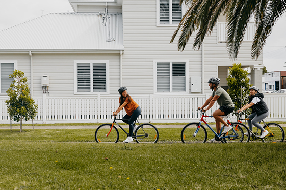 Three people cycling in front of a house